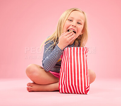Buy stock photo Popcorn eating, portrait and happy girl in a studio with pink background sitting with movie snacks. Food taste, happiness and hungry young child with a paper bag and chips feeling relax with a smile