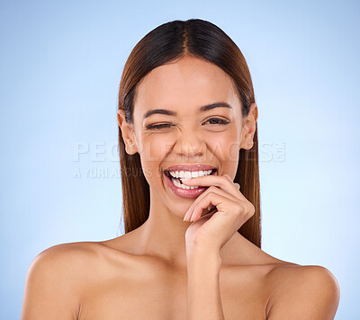 Buy stock photo Beauty, woman and biting finger and wink portrait for skincare dermatology cosmetics in studio. Female model person on blue background for self care, facial glow and healthy or clean skin with smile