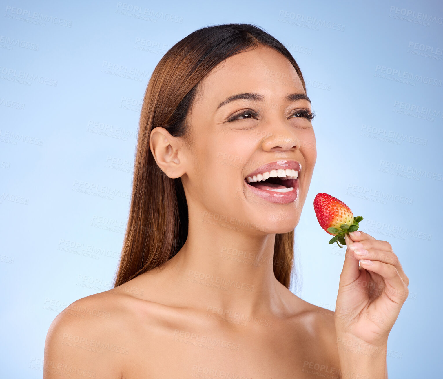 Buy stock photo Skincare, wellness and woman with a strawberry in studio with a healthy, natural and face routine. Happy, beauty and female model with dermatology facial treatment eating red fruit by blue background