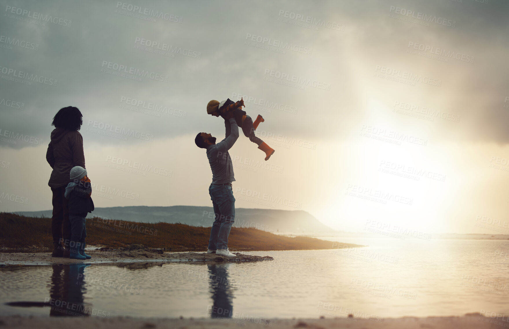 Buy stock photo Sunset, view and a playing family on the beach together on a beautiful summer evening outdoor. Earth, water or nature with a mother, father and children bonding by the ocean or sea at the coast