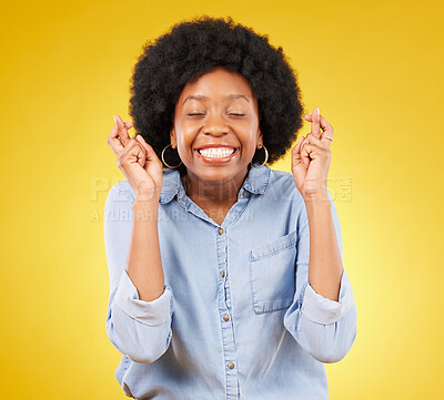 Buy stock photo Happy, smile and fingers crossed by black woman in studio for wish, hope and good luck against yellow background. Eyes closed, hand and emoji by excited female waiting, optimistic and hopeful gesture