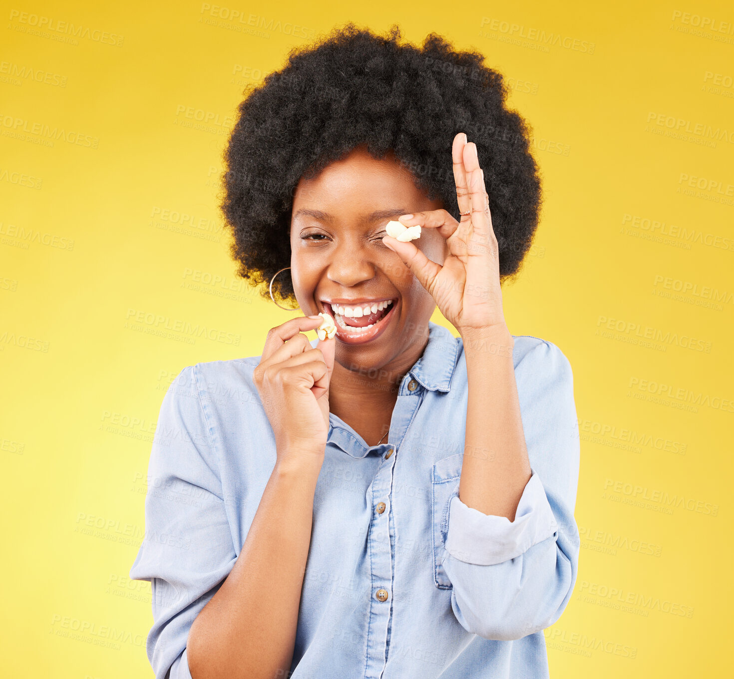 Buy stock photo Black woman, funny face and eating popcorn in studio isolated on a yellow background. Comic smile, food and portrait of laughing, hungry and happy, goofy or silly female playing with corn or snack.