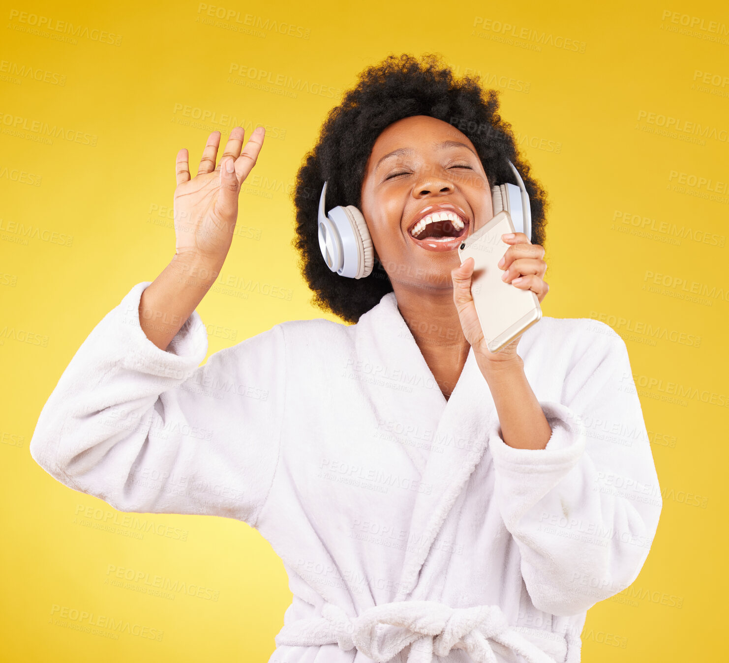 Buy stock photo Black woman, music headphones and singing with phone in studio isolated on a yellow background. Karaoke singer, bathrobe and happy female dance with mobile microphone while streaming podcast or radio