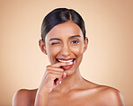 Flirty, beauty and portrait of a winking woman isolated on a studio background. Happy, sexy and face of an Indian model with makeup, cosmetics and attitude on a backdrop to advertise lipstick