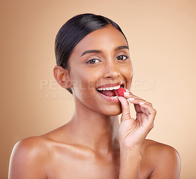 Buy stock photo Portrait, beauty and woman biting a strawberry in studio on a beige background to promote skincare. Face, fruit and eating with an attractive young female posing for organic or natural cosmetics