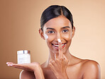 Portrait, product and nose with a model woman in studio on a beige background to apply facial lotion. Face, beauty and skincare with an attractive young female applying moisturizer to her skin