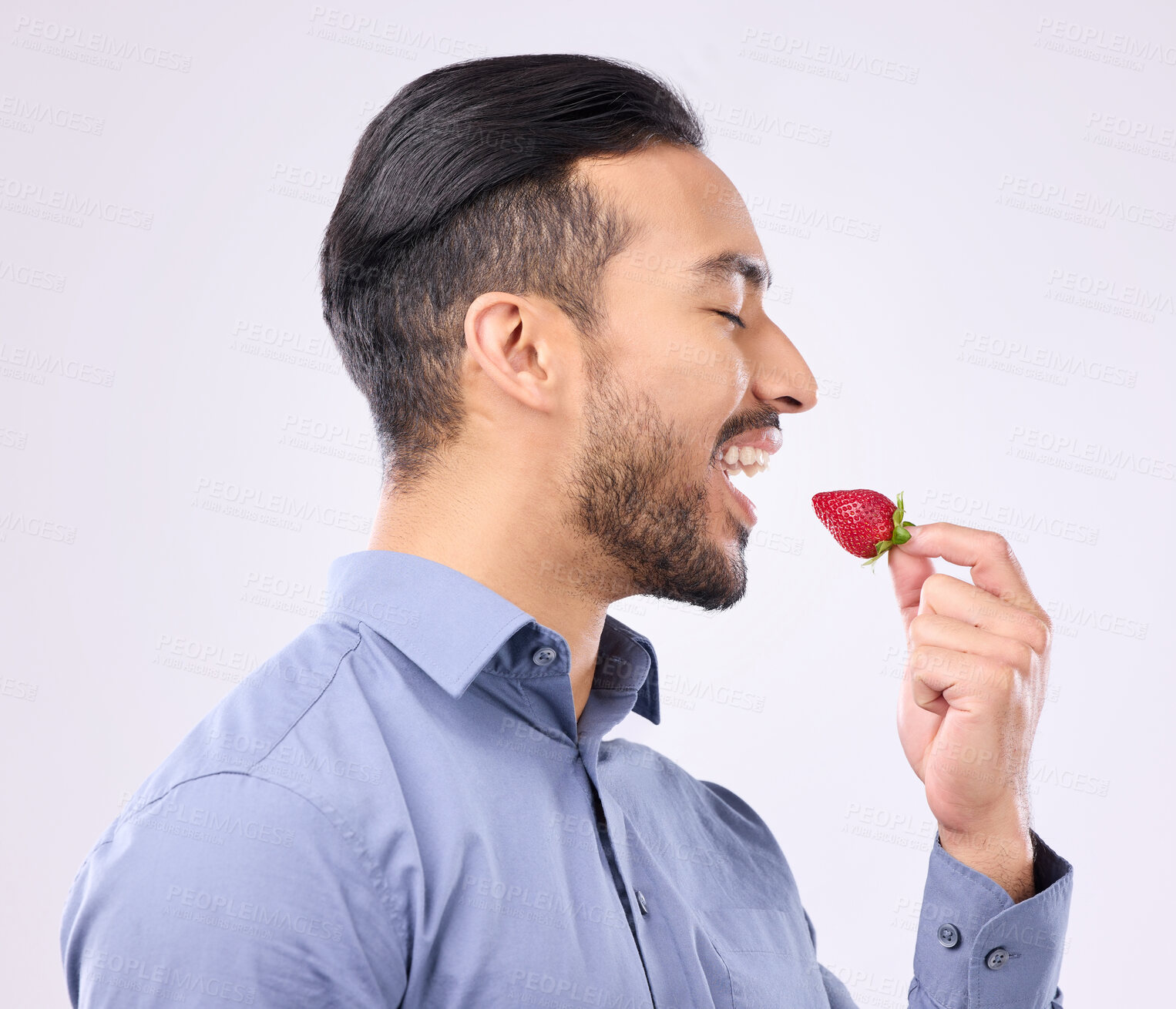 Buy stock photo Healthy, diet and a man eating a strawberry in studio on a gray background for natural nutrition. Food, fruit and vegan with a handsome young male biting a red, juicy or tasty berry for dessert