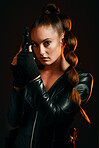 Portrait, gun and spy with a woman assassin in studio on a dark background ready for combat. Hero, leather and power with an attractive young female secret agent holding a weapon on a mission