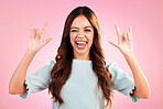 Portrait of woman, rock hand gesture and wink in studio, heavy metal expression on face and pink background. Crazy, wild hispanic model and hands in devil horn sign with punk attitude and happy smile