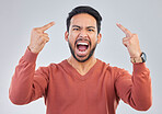 Angry, middle finger and portrait of asian man in studio for rude, conflict and problem. Annoyed, upset and aggressive with male and hand gesture on gray background for hate, disrespect and furious