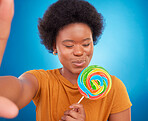 Woman, rainbow lollipop and selfie in studio with a smile and happiness or lgbtq pride on face. Black female model with a color candy on a blue background with sugar, sweets or dessert while excited