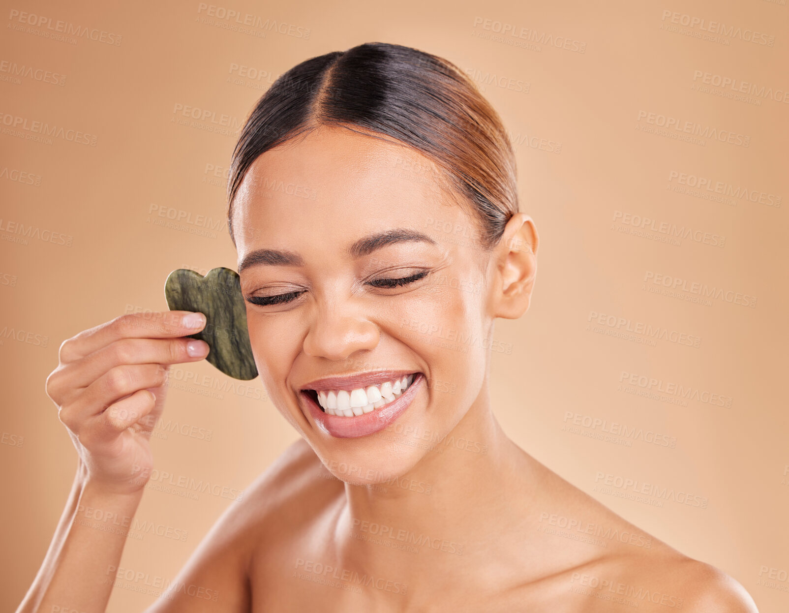 Buy stock photo Happy, facial and massage with gua sha by woman in studio for skincare, cosmetics and facelift on brown background. Smile, face and anti aging tool for girl beauty model relax with luxury dermatology