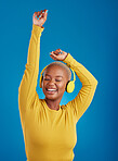 Black woman with headphones, dance and listen to music with rhythm and fun with freedom on blue background. Happy female with arms raised, streaming radio with dancing and carefree in studio