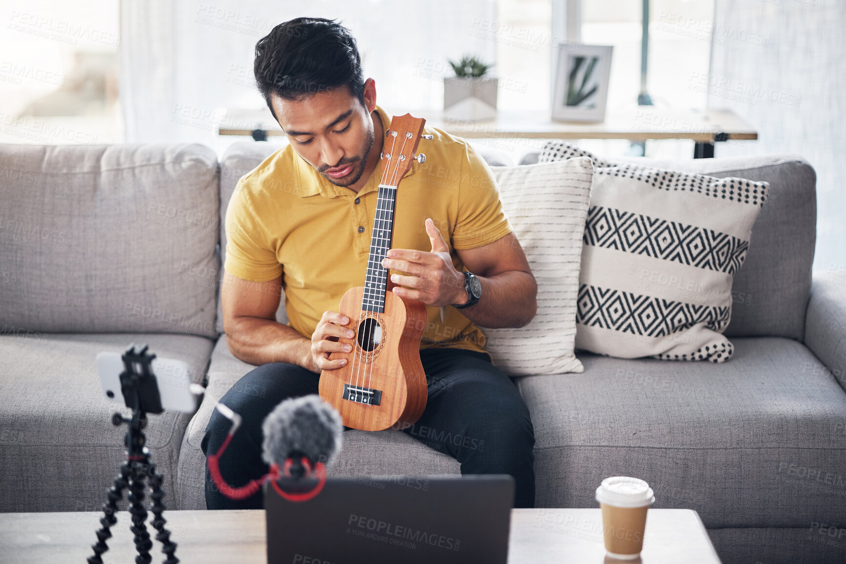 Buy stock photo Guitar, podcast and phone with a man online teaching, show and coach on live streaming lesson. Asian male person happy on home sofa with a ukulele as content creator teaching music on education blog