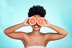 Black woman, face and smile with grapefruit for skincare nutrition, beauty or vitamin C against a blue studio background. Portrait of African female smiling with fruit for natural health and wellness