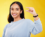 Showing, small and portrait of a woman with hands isolated on a yellow background in a studio. Happy, measurement and a girl with a review, gesturing size and opinion with fingers on a backdrop