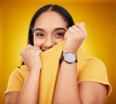 Buy stock photo Portrait, shy and funny with a woman on a yellow background in studio pulling on her t-shirt. Face, fashion or playful and an attractive young female covering her mouth with trendy clothes for style
