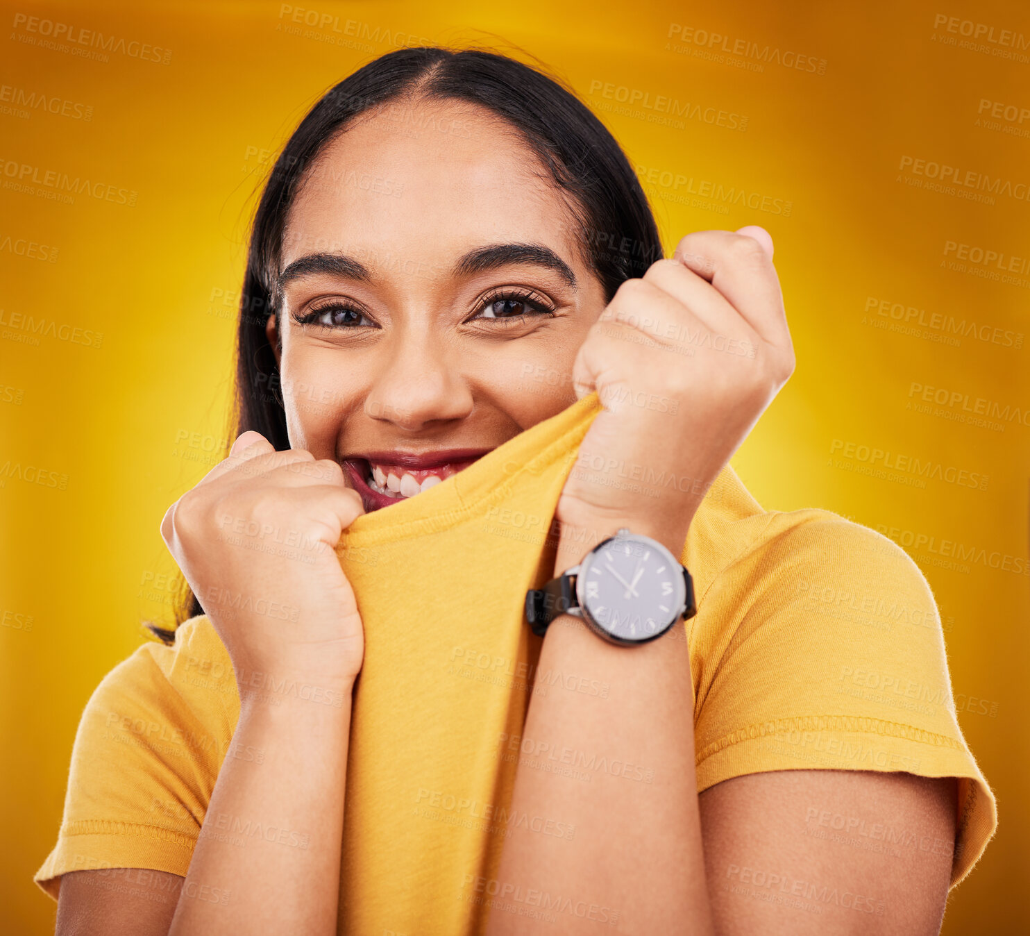 Buy stock photo Portrait, shy and playful with a woman on a yellow background in studio pulling on her t-shirt. Face, fashion or funny and an attractive young female covering her mouth with trendy clothes for style