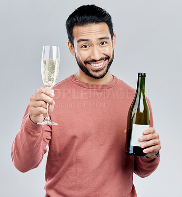 Buy stock photo Portrait, champagne and toast with a man in studio on a gray background holding a bottle for celebration. Glass, alcohol and cheers with a handsome young man celebrating the new year tradition