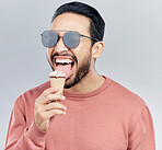 Summer, sunglasses and ice cream with a man in studio on a gray background enjoying a sweet, treat or snack. Food, fashion and dessert with a handsome young male eating or licking an icecream cone 