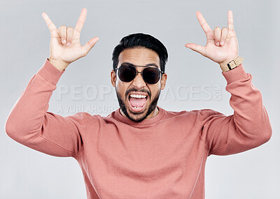 Buy stock photo Portrait, rocker and hand gesture with a man in studio on a gray background feeling crazy or energetic. Face, rock on or hardcore and a male posing with a devil horns sign or symbol at a concert