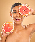 Face smile, skincare and woman with grapefruit in studio isolated on a brown background. Portrait, natural cosmetics and happy Indian female model with citrus fruit for vitamin c, nutrition or beauty