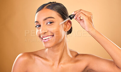 Buy stock photo Face portrait, skincare serum and woman in studio isolated on brown background. Dermatology, cosmetics and smile of Indian female model with hyaluronic acid, retinol or essential oil for healthy skin
