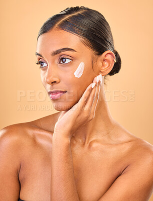 Buy stock photo Face, beauty skincare and woman with cream in studio isolated on a brown background. Dermatology, cosmetics idea and thinking Indian female model with lotion, creme or moisturizer for skin health.