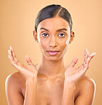 Face portrait, skincare and woman with cream in studio isolated on a brown background. Dermatology smile, cosmetics and happy Indian female model apply lotion, creme and moisturizer for healthy skin.