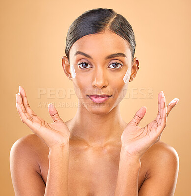 Buy stock photo Face portrait, skincare and woman with cream in studio isolated on a brown background. Dermatology, cosmetics and serious Indian female model apply lotion, creme and moisturizer for healthy skin.