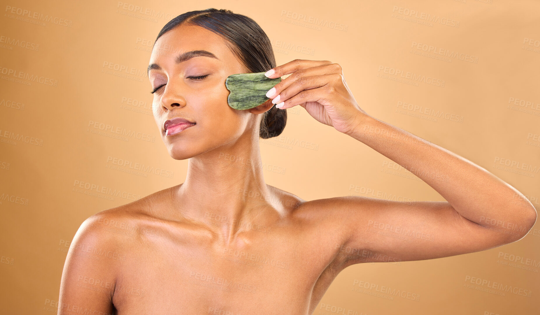 Buy stock photo Face, skincare stone and woman with eyes closed in studio isolated on a brown background. Dermatology, facial massage and Indian female model with jade crystal or gua sha for healthy skin treatment.