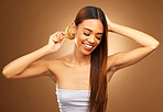 Brushing hair, beauty and a woman happy in studio for growth and color shine or healthy texture. Aesthetic female smile for haircare, natural self care and hairdresser or salon on brown background
