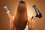 Hair, brush and hairdryer of woman in studio for growth and color shine or healthy texture. Aesthetic female hands with tools for haircare, self care and hairdresser or salon on brown background
