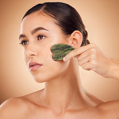 Buy stock photo Beauty, gua sha and face of woman for skincare, facial treatment and wellness with spa stone. Salon, dermatology and girl on brown background with cosmetics, face massage and luxury tools in studio