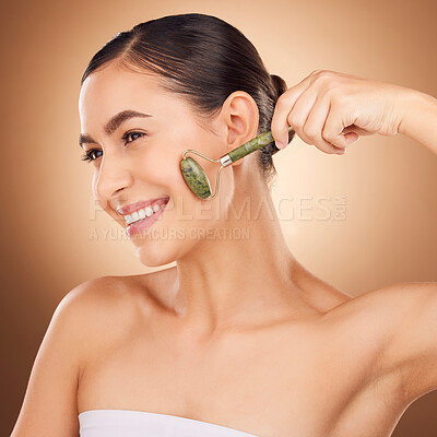 Buy stock photo Jade roller, skincare and happy woman in studio for beauty, wellness and anti aging against brown background. Facial, skin and girl relax with massaging tool, facelift and lymphatic drainage isolated