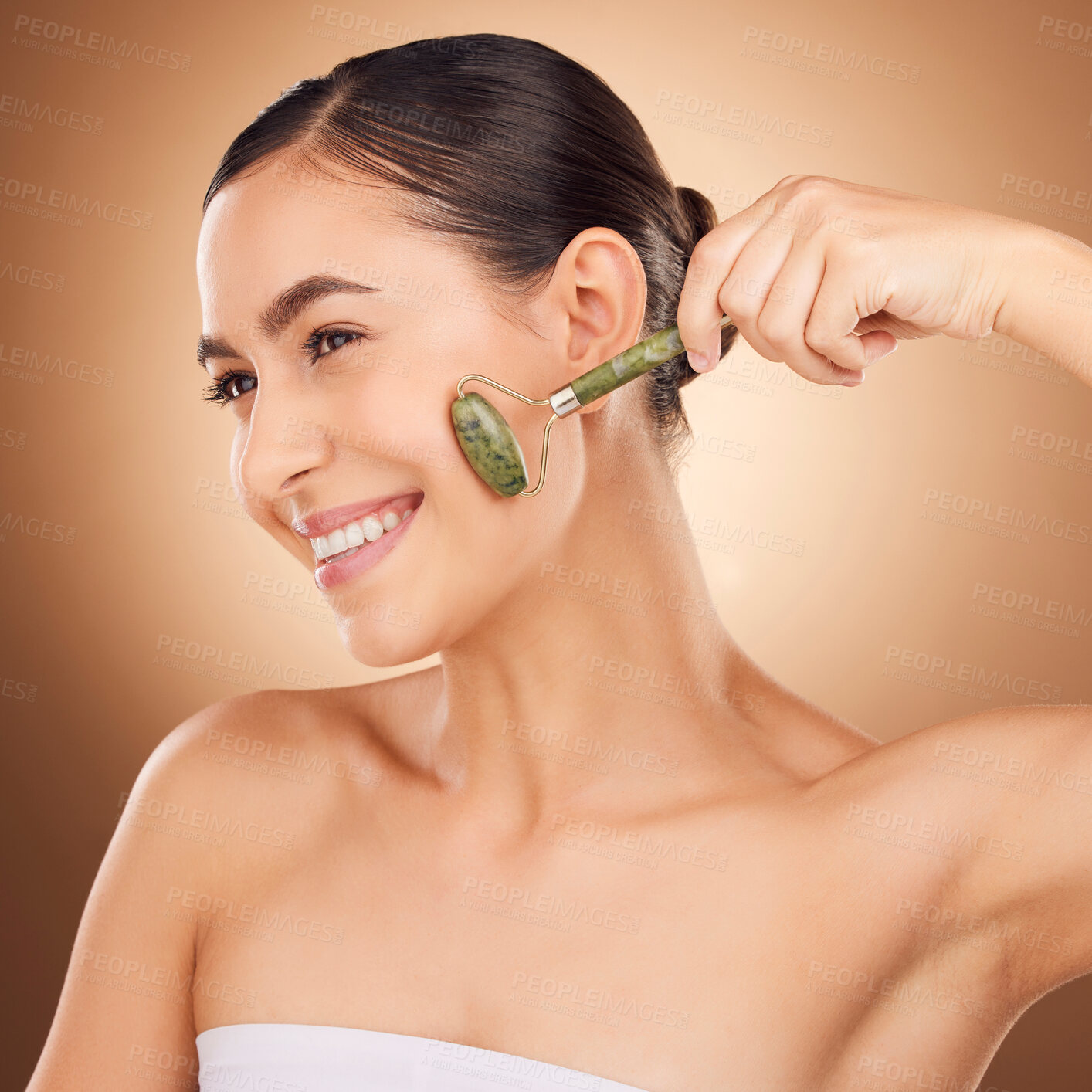 Buy stock photo Jade roller, skincare and happy woman in studio for beauty, wellness and anti aging against brown background. Facial, skin and girl relax with massaging tool, facelift and lymphatic drainage isolated