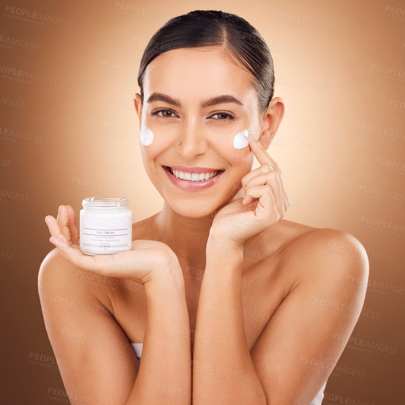 Buy stock photo Portrait, skincare and lotion with a model woman in studio on a brown background for beauty or hydration. Face, skin and cream with a happy young female holding a container to apply moisturizer