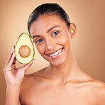 Portrait, beauty and avocado with a model woman in studio on a brown background for natural treatment. Face, food and antioxidants with an attractive young female holding healthy fruit for nutrition