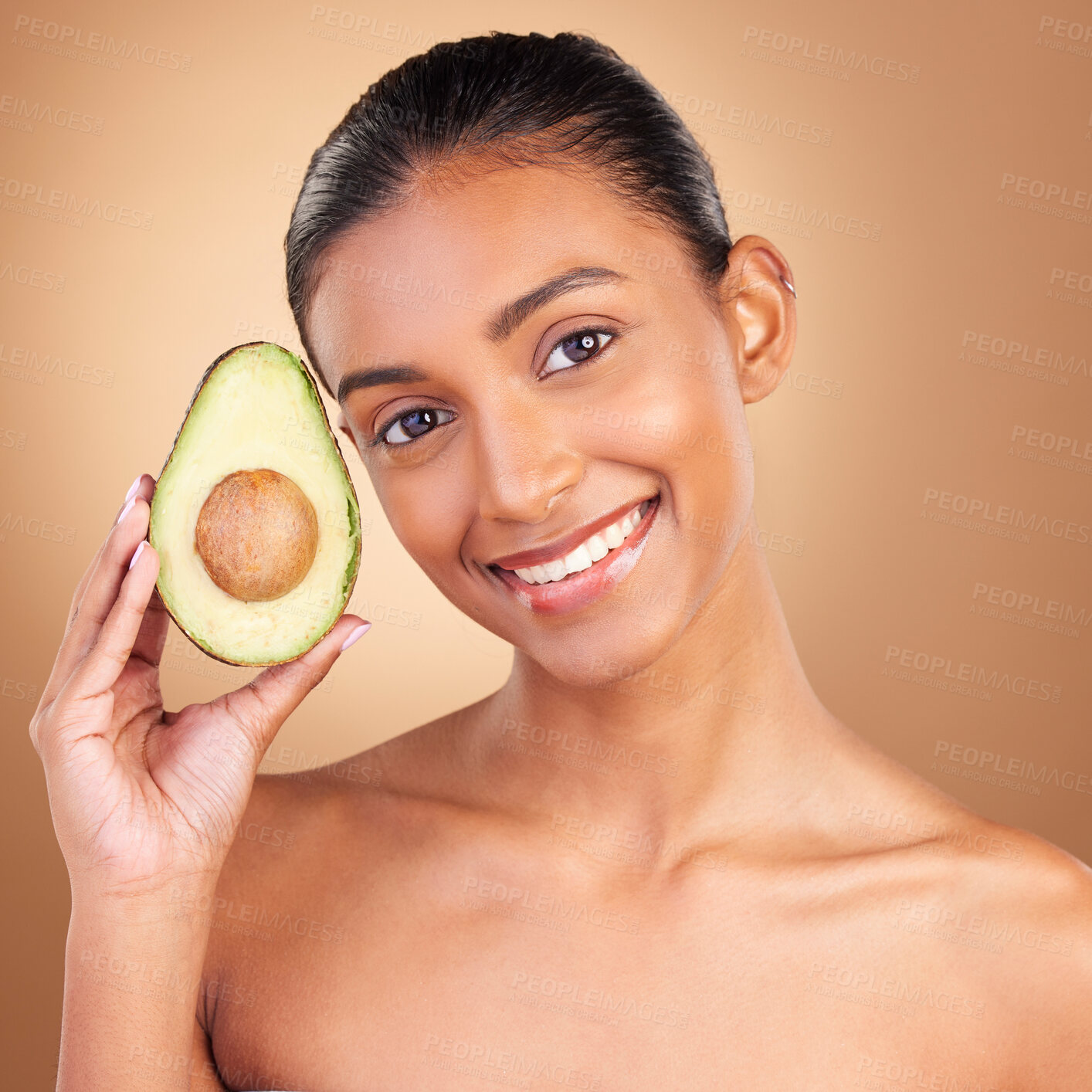 Buy stock photo Portrait, beauty and avocado with a model woman in studio on a brown background for natural treatment. Face, food and antioxidants with an attractive young female holding healthy fruit for nutrition