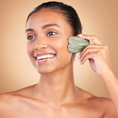 Buy stock photo Beauty, gua sha and face of Indian woman for skincare, facial treatment and wellness with spa tools. Salon, dermatology and happy girl on brown background for cosmetics, face massage and luxury stone