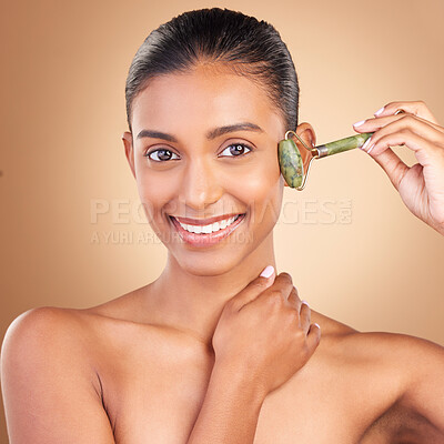 Buy stock photo Portrait, massage and skincare with a model woman in studio on a brown background for natural antiaging beauty. Face, luxury and product with an attractive young female using a roller for skin lift