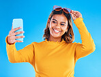 Woman, face and smile for selfie, social media or vlog in happiness and style against a blue studio background. Happy isolated female influencer smiling with teeth for photo, memory or online post