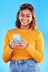 Woman, phone and smile for social media, communication or chatting isolated against a blue studio background. Happy female smiling with teeth texting on mobile smartphone in happiness for online chat