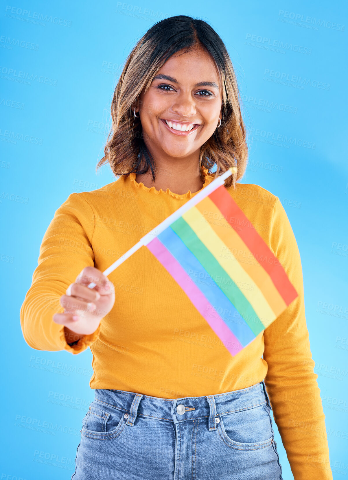 Buy stock photo Portrait, flag and gay pride with a woman on a blue background in studio feeling proud of her lgbt status. Smile, freedom and equality with a happy young female holding a symbol of inclusion