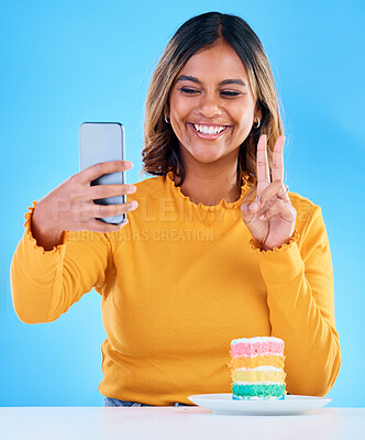 Buy stock photo Woman, cake and peace selfie in studio for social media with a smile and excited to eat. Happy, female person and hand emoji on blue background with rainbow color dessert for birthday celebration