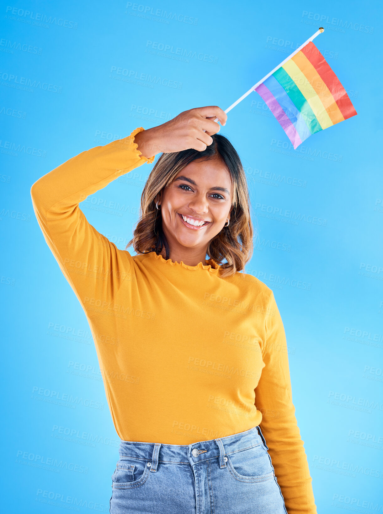 Buy stock photo Portrait, rainbow flag and gay pride with a woman on a blue background in studio feeling proud of her lgbt status. Smile, freedom and equality with a happy young female holding a symbol of inclusion