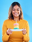 Birthday cake, happy party and woman in studio, blue background and celebration. Female model, rainbow dessert and candle of special event, sweets and smile to celebrate happiness, wish and surprise