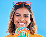 Portrait, lollipop and a woman smiling on a blue background in studio wearing heart glasses for fashion. Face, candy and sweet with a happy young female eating a giant snack while feeling positive