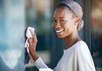 Maid, housekeeper and black woman cleaning and wipe a glass window for hygiene doing housework or chores. Smile, happy and portrait of female cleaner working in a house with detergent to disinfect