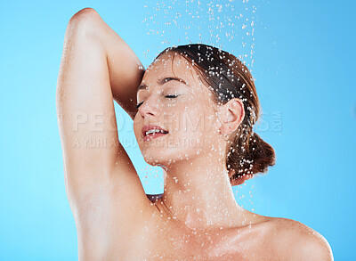 Buy stock photo Water, shower and woman cleaning her body as skincare, dermatology and self care isolated in a studio blue background. Aqua, beauty and female model washing her skin for wellness while feeling calm